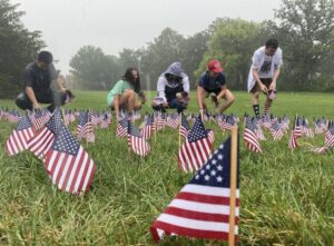 People placing American flags on lawn in rain.