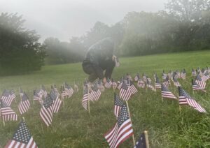 Person placing flags in grass on misty day.